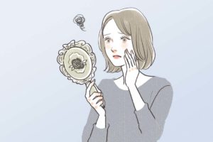 鏡を見て目尻のシワにうんざりしている女性